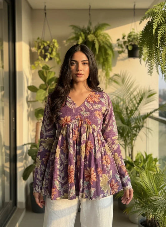 Woman wearing a purple floral cotton kurti with long sleeves, standing on a balcony with green plants.