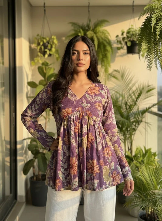 Woman in a purple floral cotton kurti with long sleeves and white pants, standing on a balcony with green plants