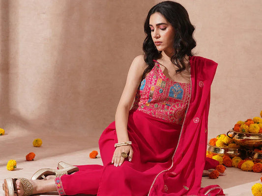 Woman in bright pink ethnic kurta set with embroidered dupatta, sitting among marigold flowers