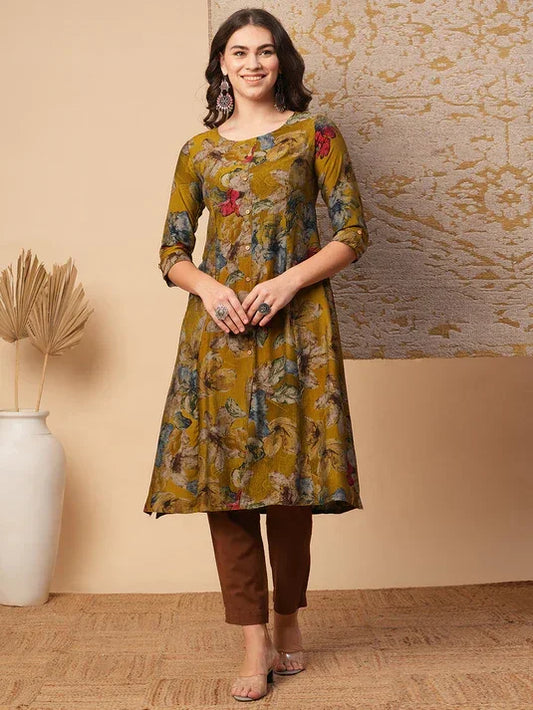 Woman wearing mustard floral printed cotton kurti with brown pants, standing indoors.